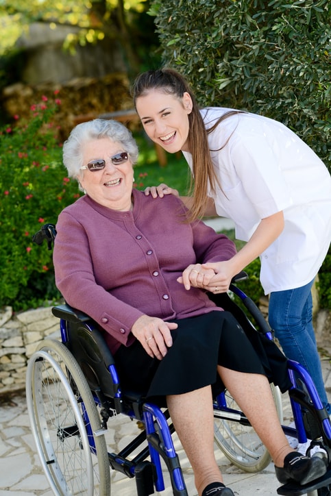 elderly senior woman on wheelchair with nurse companion outside home in garden