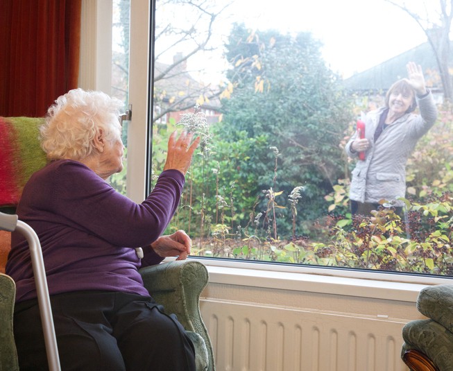An independent living elderly client waving goodbye to her home care professional through the window of her property